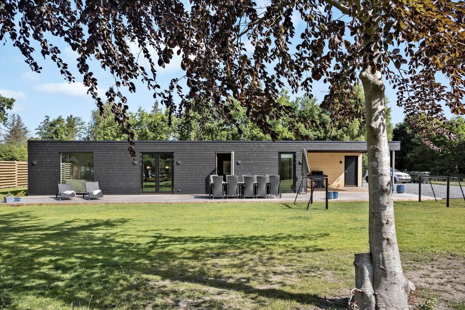 Moderne Villa mit Terrasse, Garten und Grillplatz unter Bäumen.
