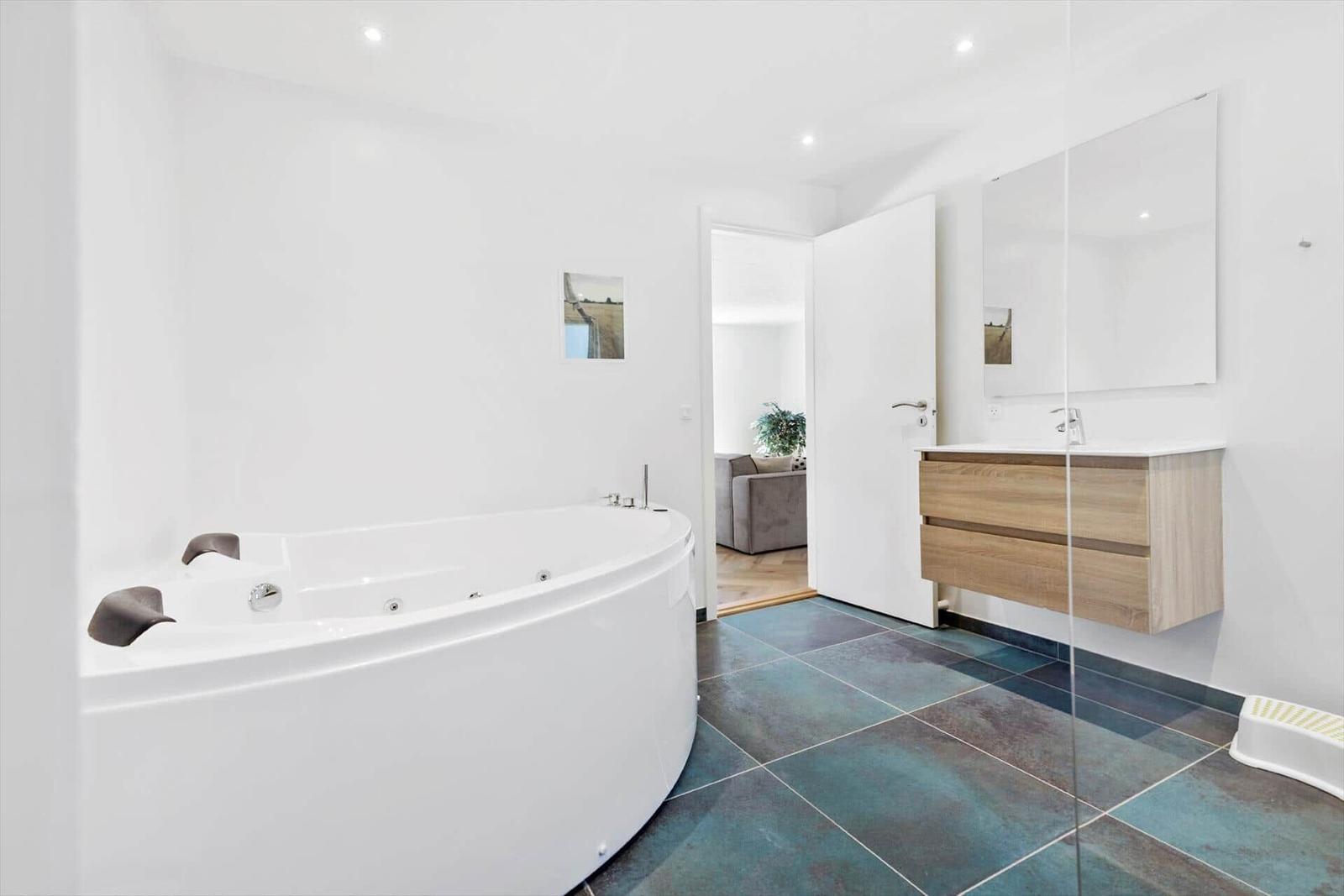 Bad mit Whirlpool, Waschtisch und Spiegel. Durchgang zur Wohnfläche.