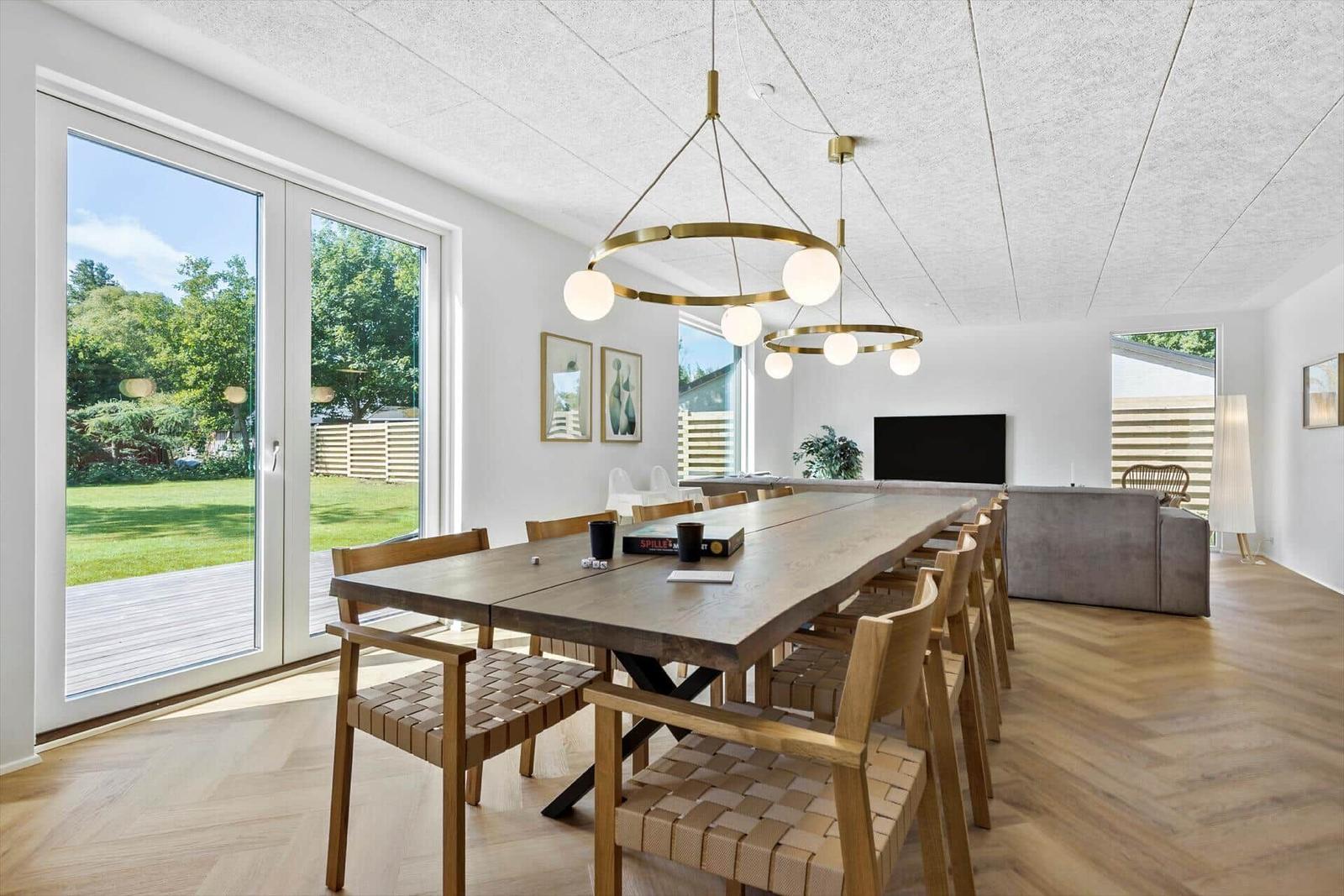 Essbereich mit langem Holztisch und Stühlen. Große Fenster mit Blick auf Garten.