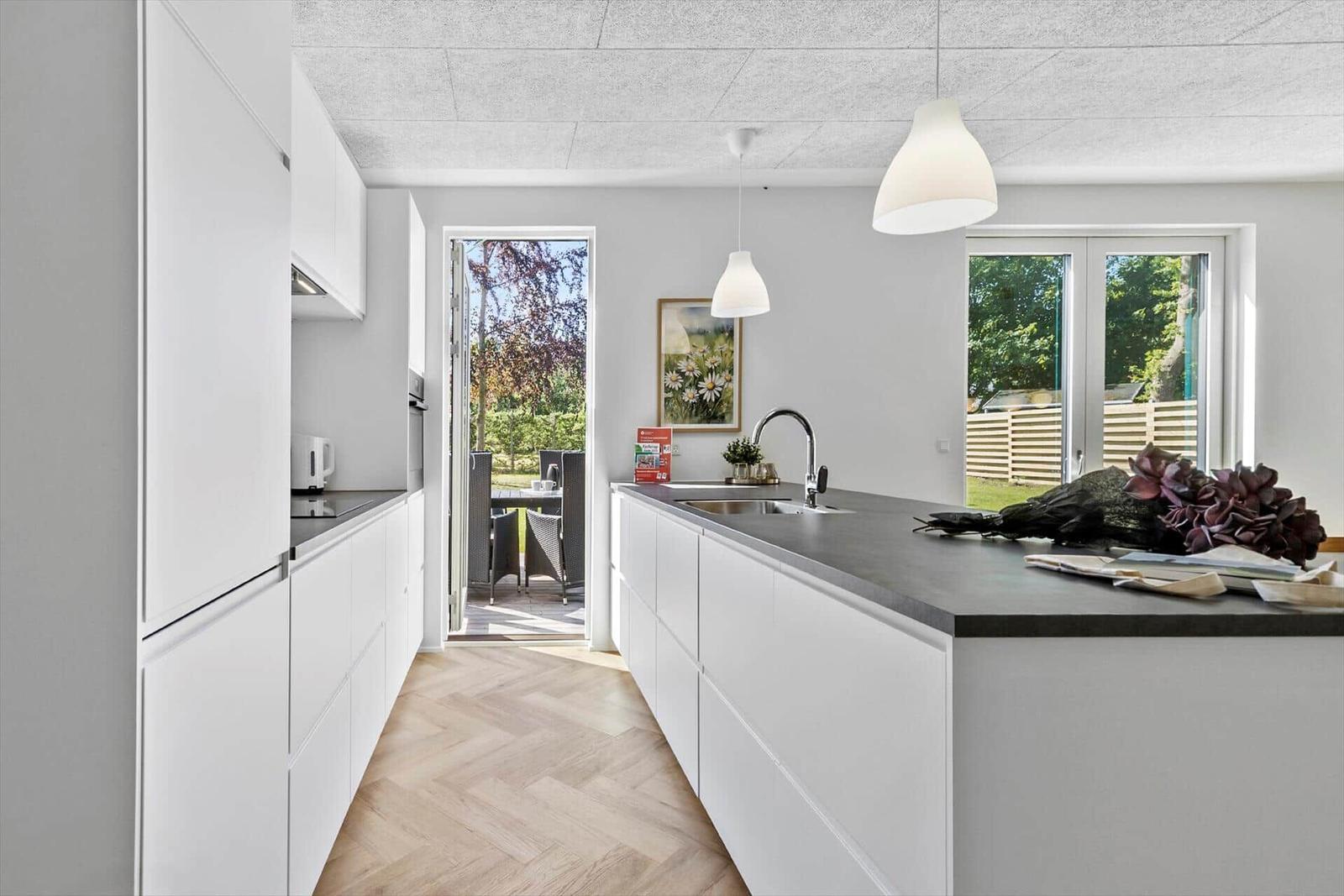 Moderne Küche mit weißen Schränken und dunklem Arbeitsplatz. Durchgang zur Terrasse mit Gartenblick.