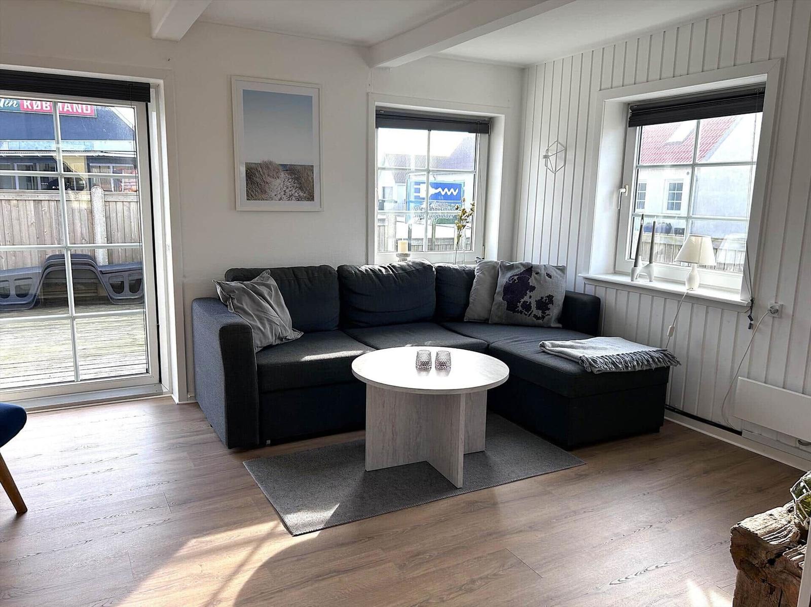 Ein Wohnzimmer mit einem schwarzen Sofa, einem runden Tisch und Fenstern mit Blick nach draußen.