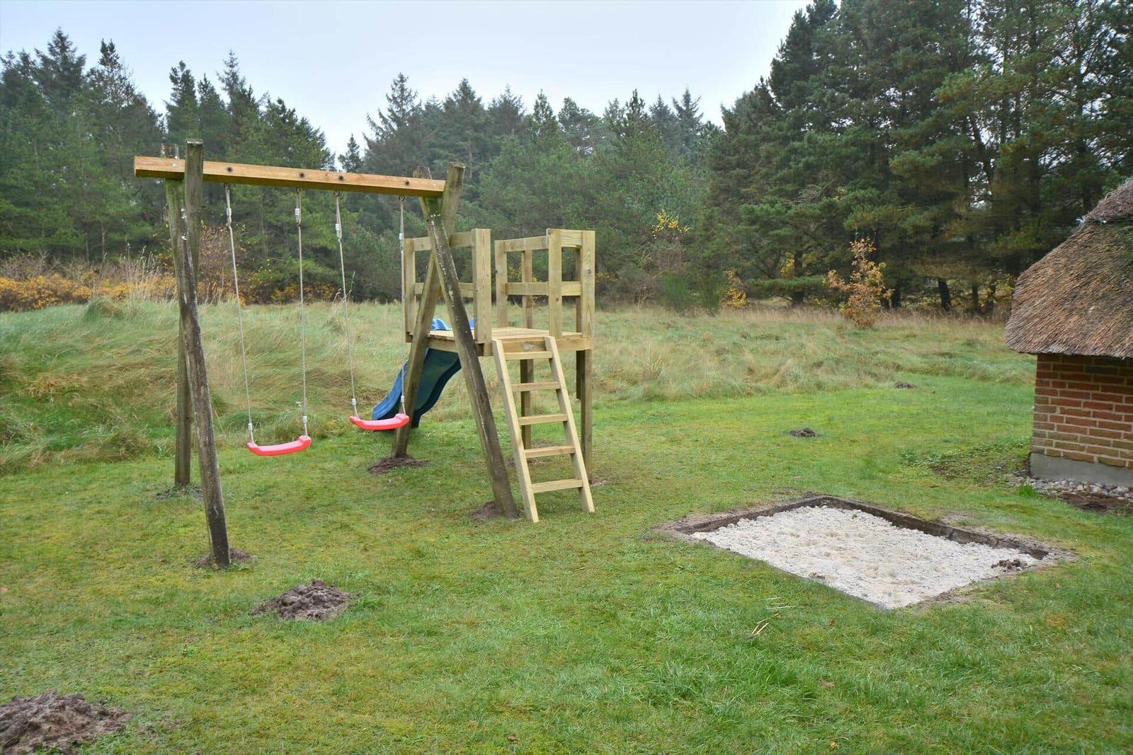 Holzspielplatz mit Schaukel, Rutsche und Sandkasten auf grünem Rasen.