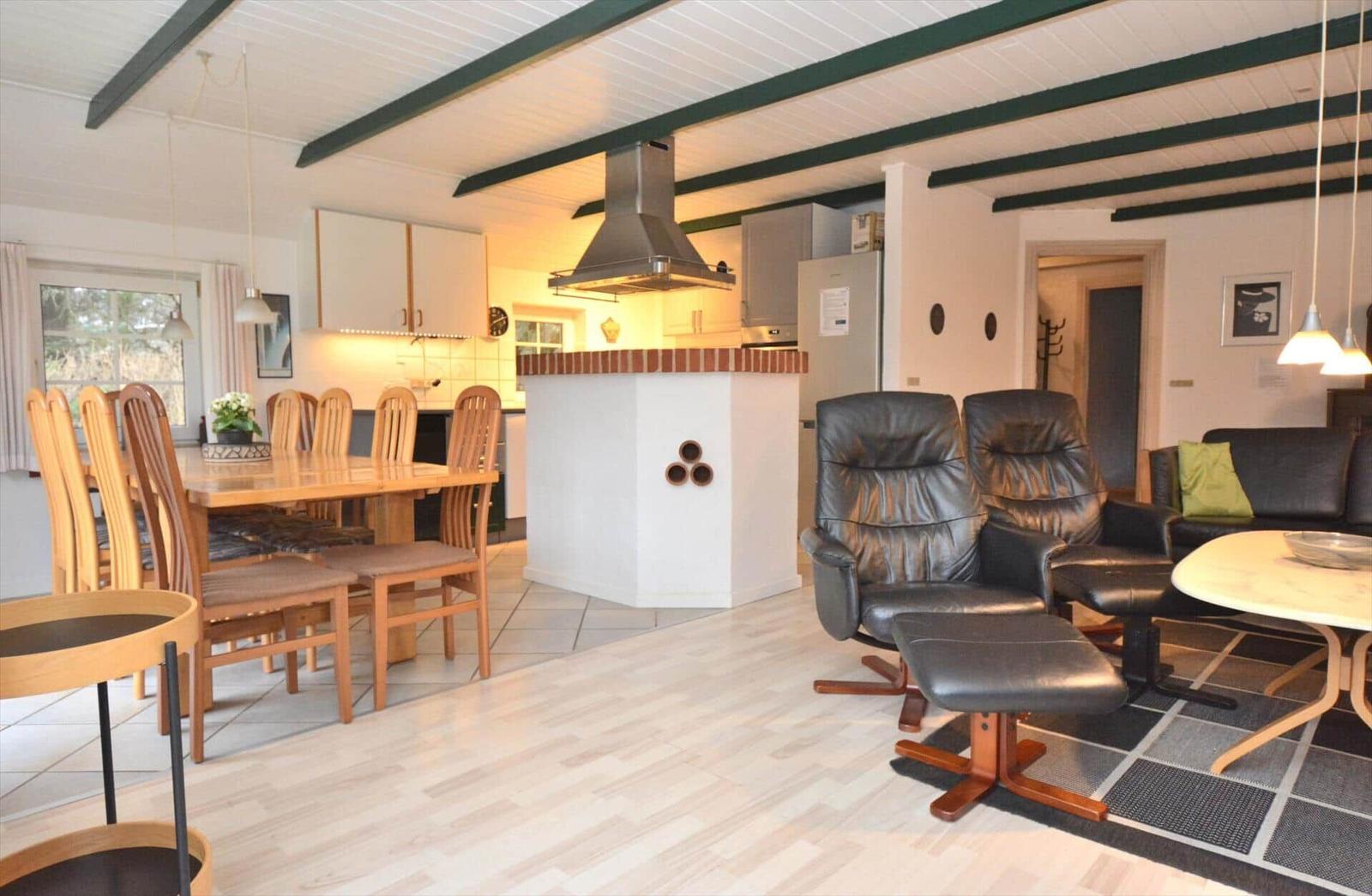 Küche mit Essbereich und Wohnzimmer mit Ledersesseln und Holzmöbeln.