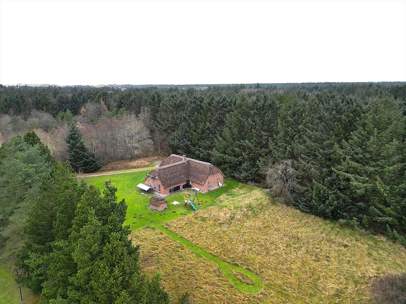 Roter Holzhaus mit Dach, umgeben von Wald und Grünfläche mit Spielplatz.