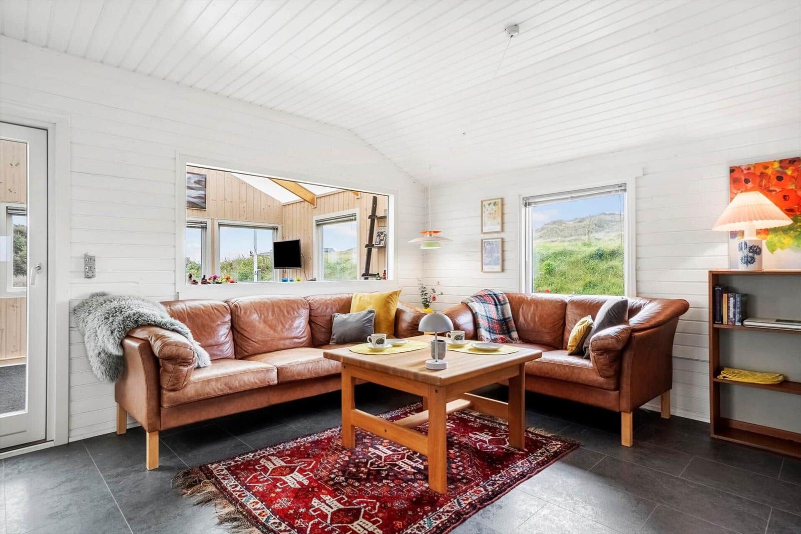 Wohnzimmer mit braunem Ledersofa, Holztisch und rotem Teppich.