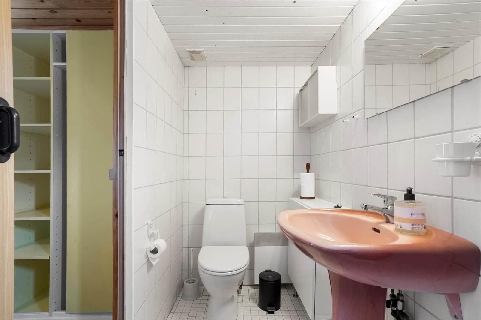 Badezimmer mit Toilette, Waschbecken und Spiegel. Weiße Fliesen und Holzdecke.