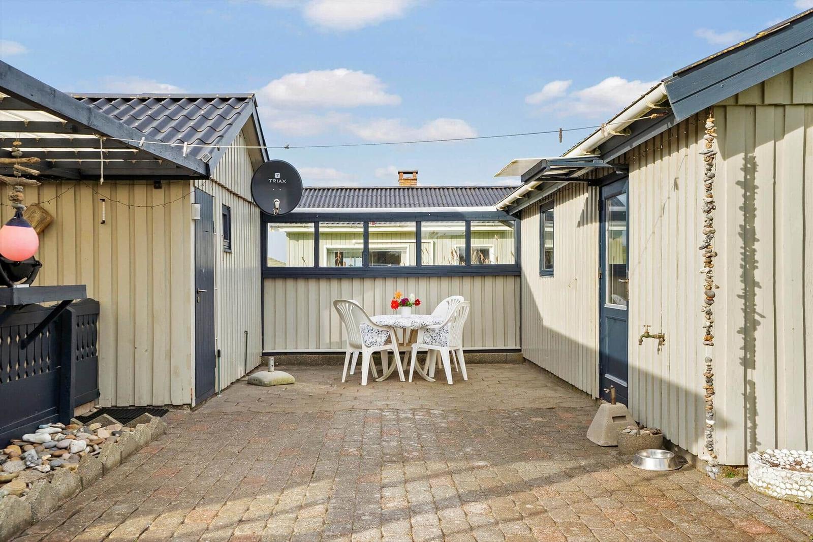 Hinterhof mit Tisch, Stühlen und Satellitenantenne. Beide Seiten sind mit Holz verkleidet.