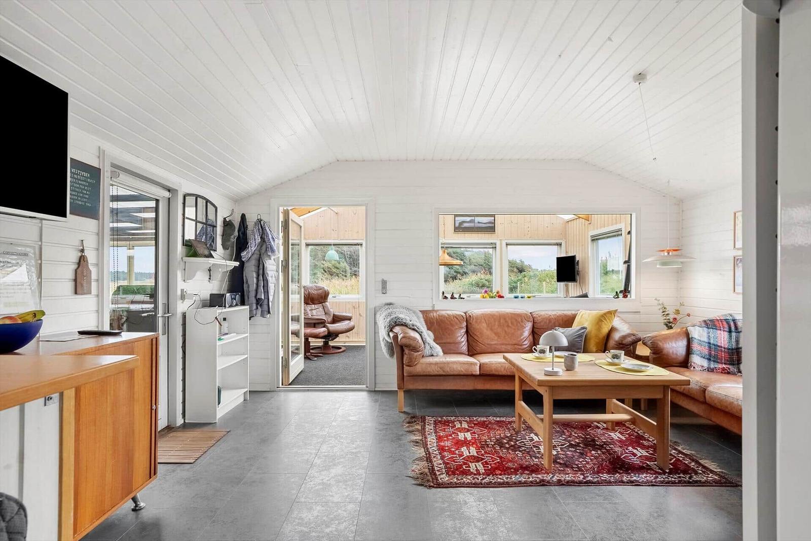 Wohnzimmer mit braunem Ledersofa, Holztisch und rotem Teppich.