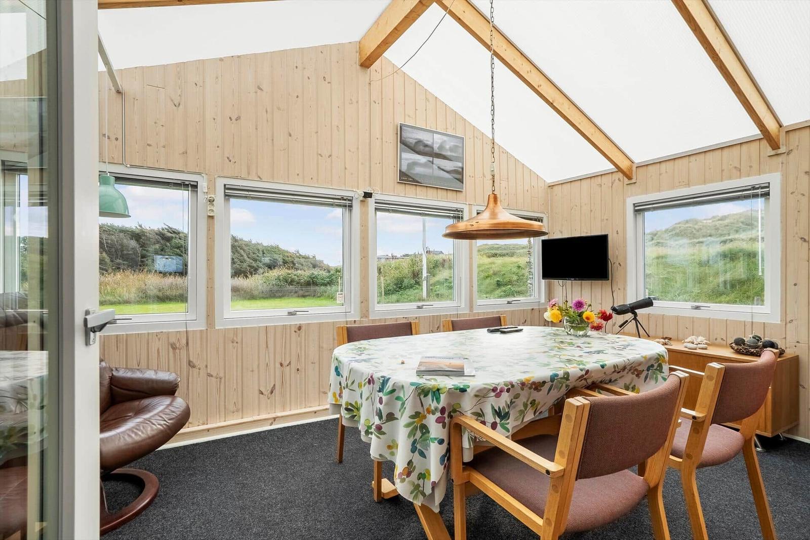 Esszimmer mit Holzwand, Tisch mit Tischdecke und Fensterblick auf Grünflächen.