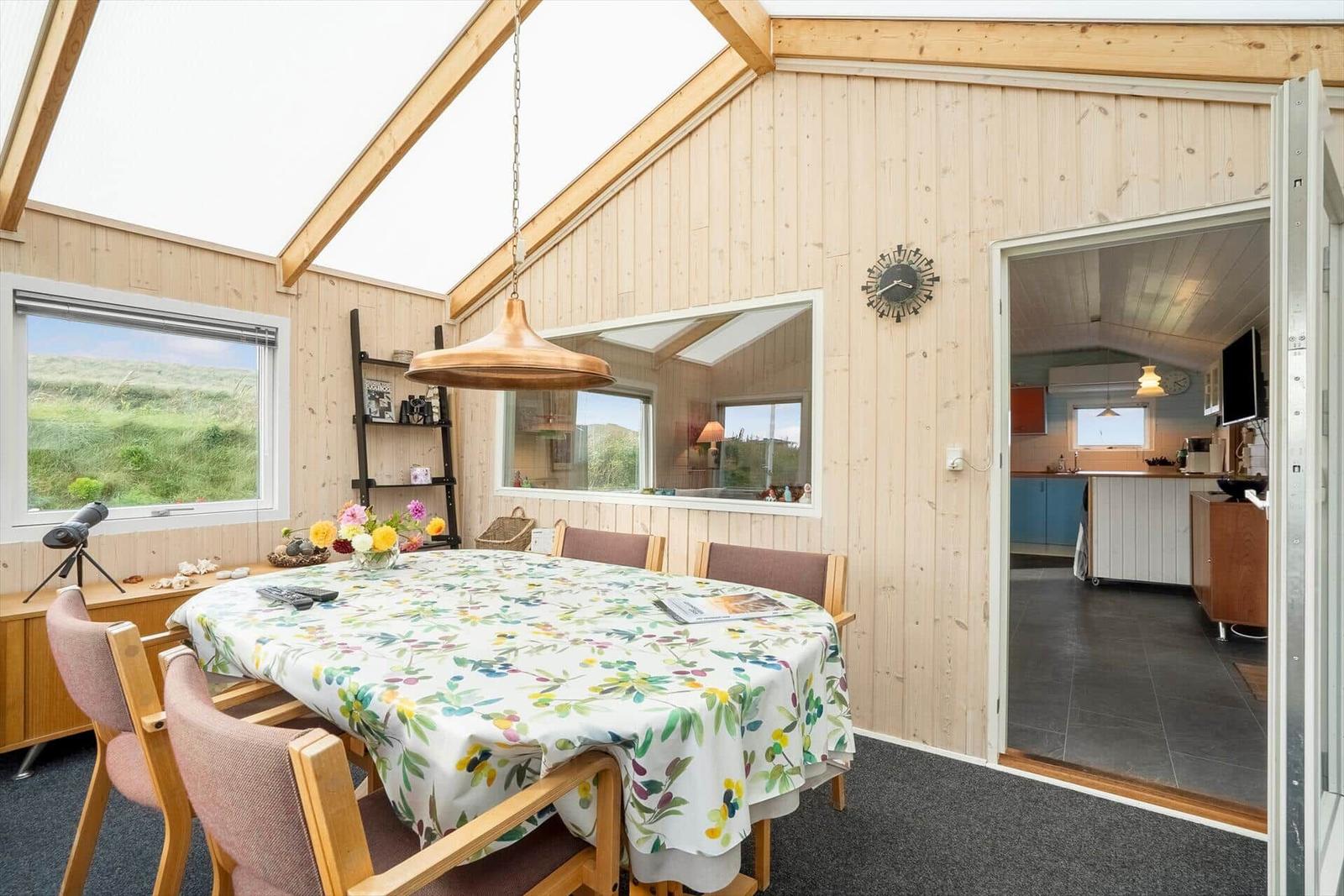 Essbereich mit Tisch, Stühlen und Blick auf Grasland. Küche ist über Tür sichtbar.