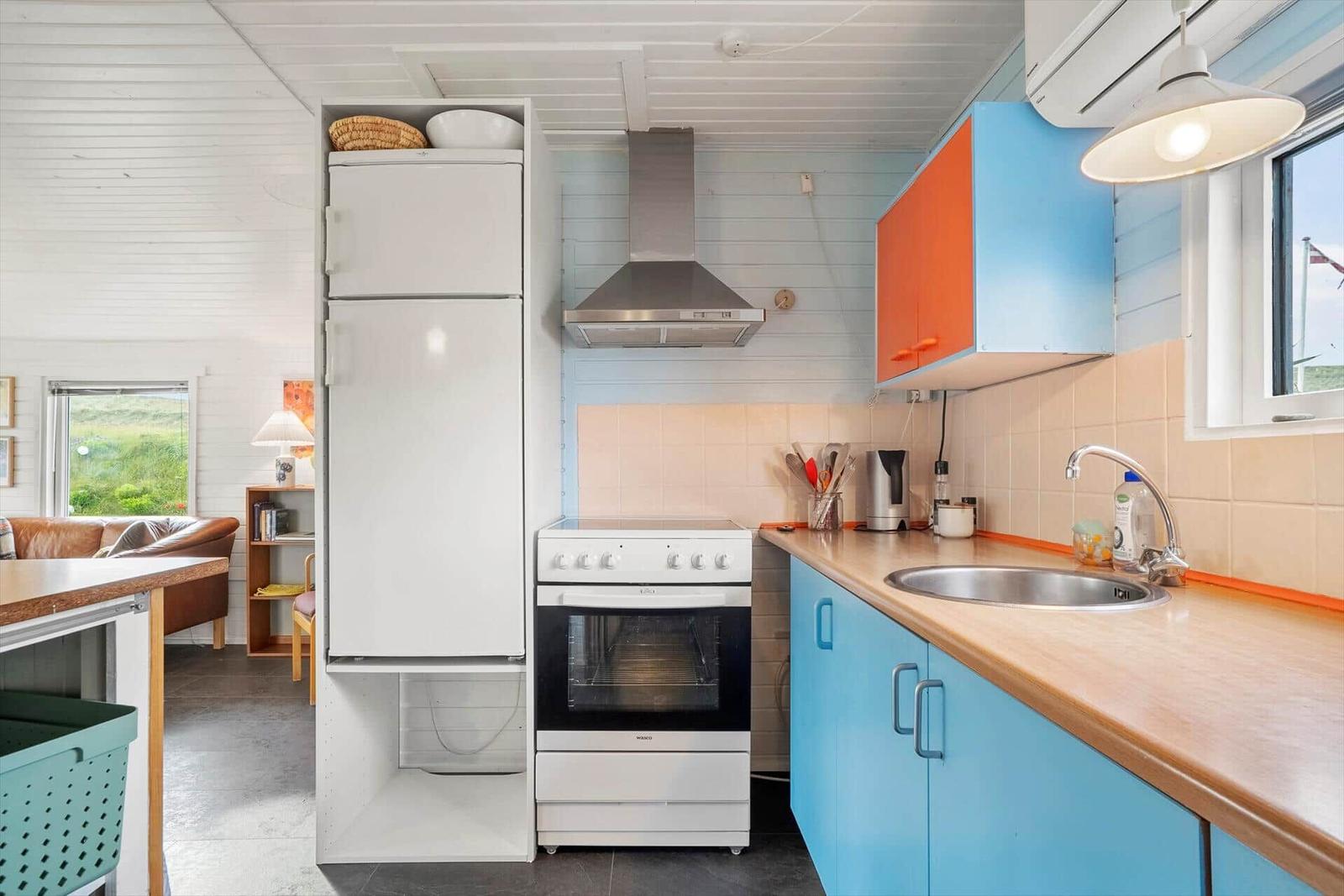 Küche mit blauen Schränken, Kühlschrank und Herd. Fenster mit Blick auf Grün.