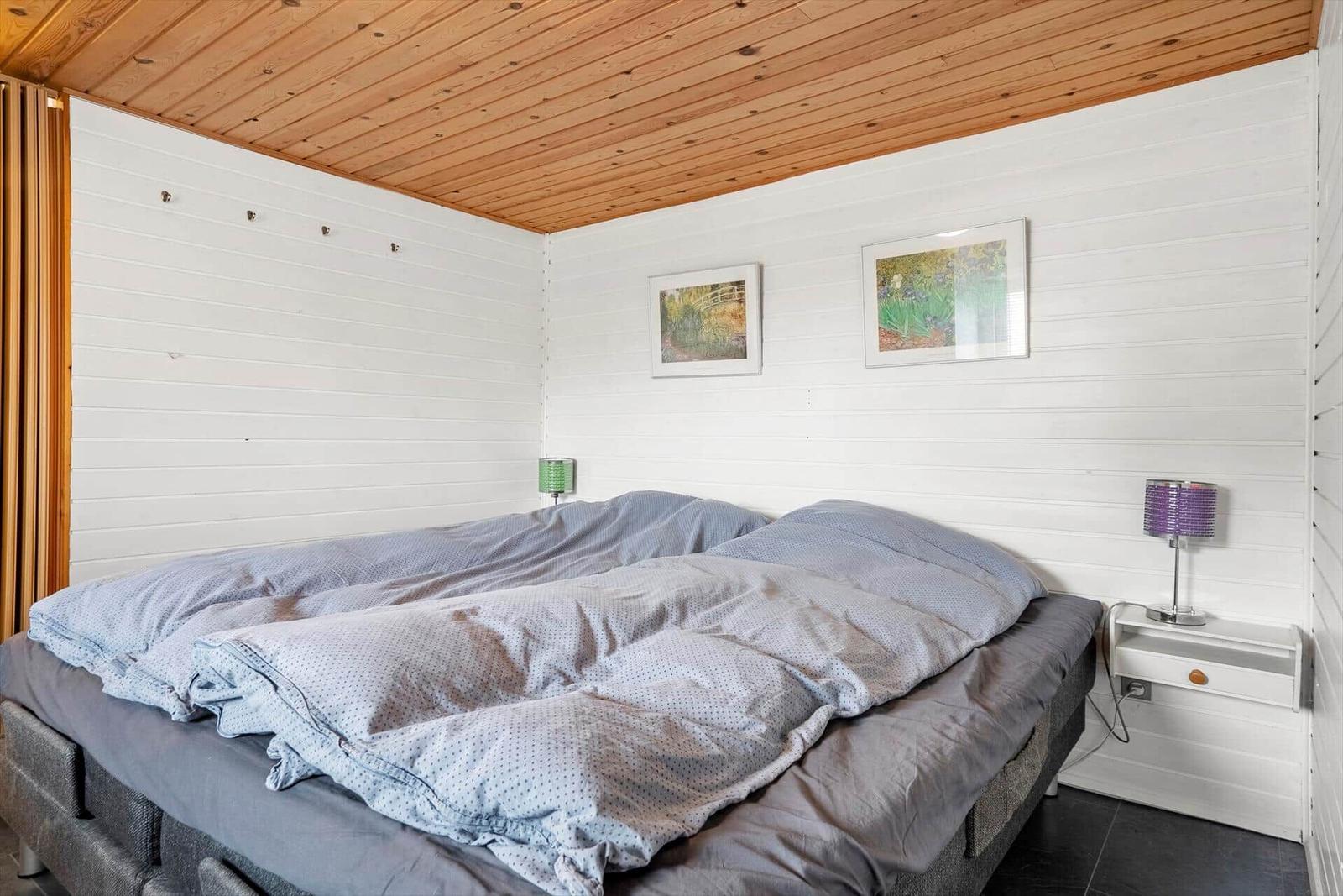 Schlafzimmer mit Doppelbett, weißen Wänden und Holzdecke. Zwei Nachttische mit Lampen.