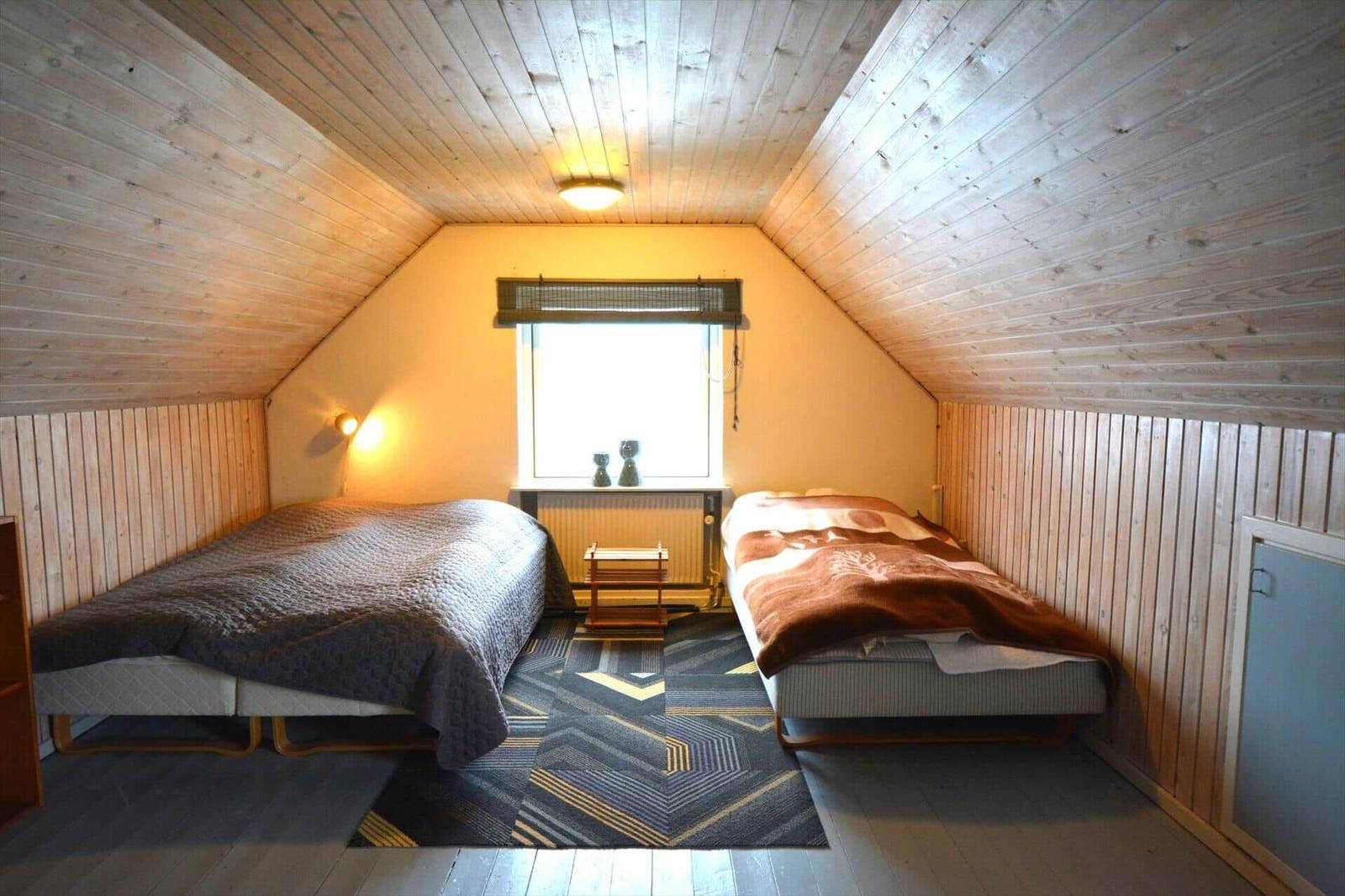 Zwei Betten in einem Dachzimmer mit Holzwand und Fenster