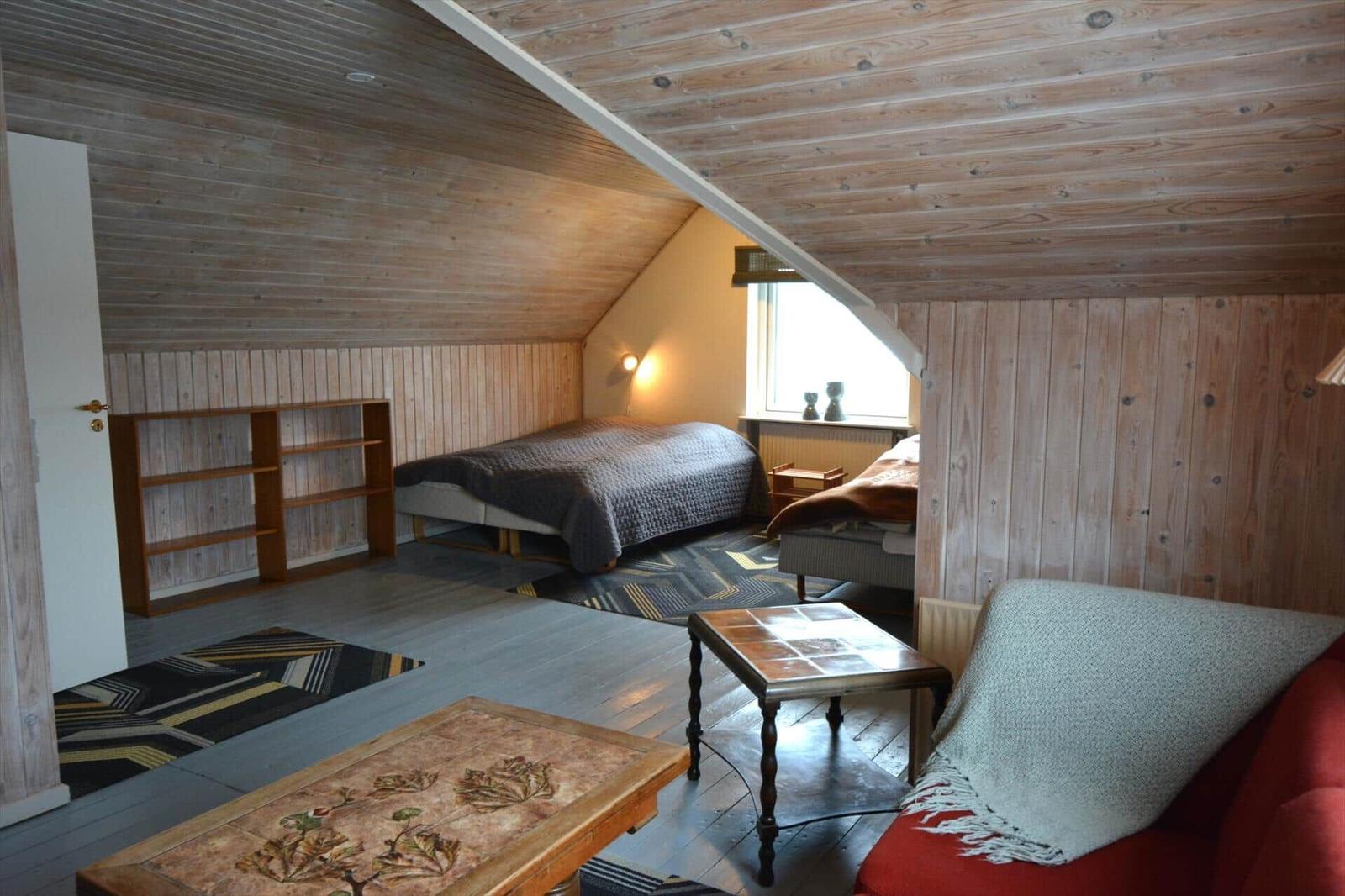 Schlafzimmer mit Holzwand, Bett, Sofa und Tisch.