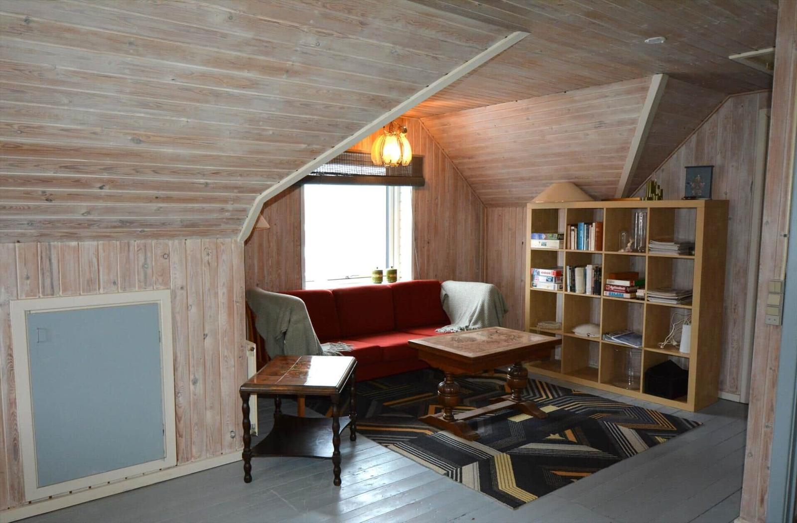 Ein Wohnzimmer mit Holzwand, rotem Sofa, Bücherregal und Holztisch.