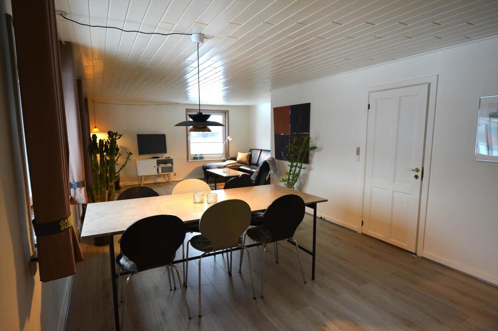Essbereich mit Tisch und Stühlen, Wohnbereich mit Sofa und Fernseher, Holzboden und weiße Wände.