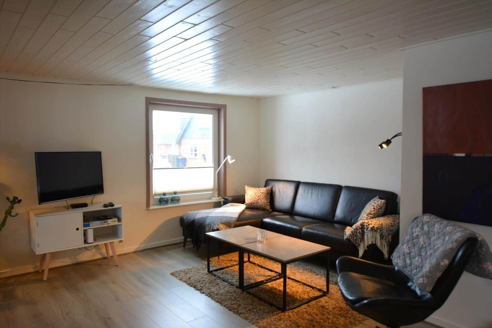 Wohnzimmer mit Sofa, Couchtisch und Fernseher an der Wand.