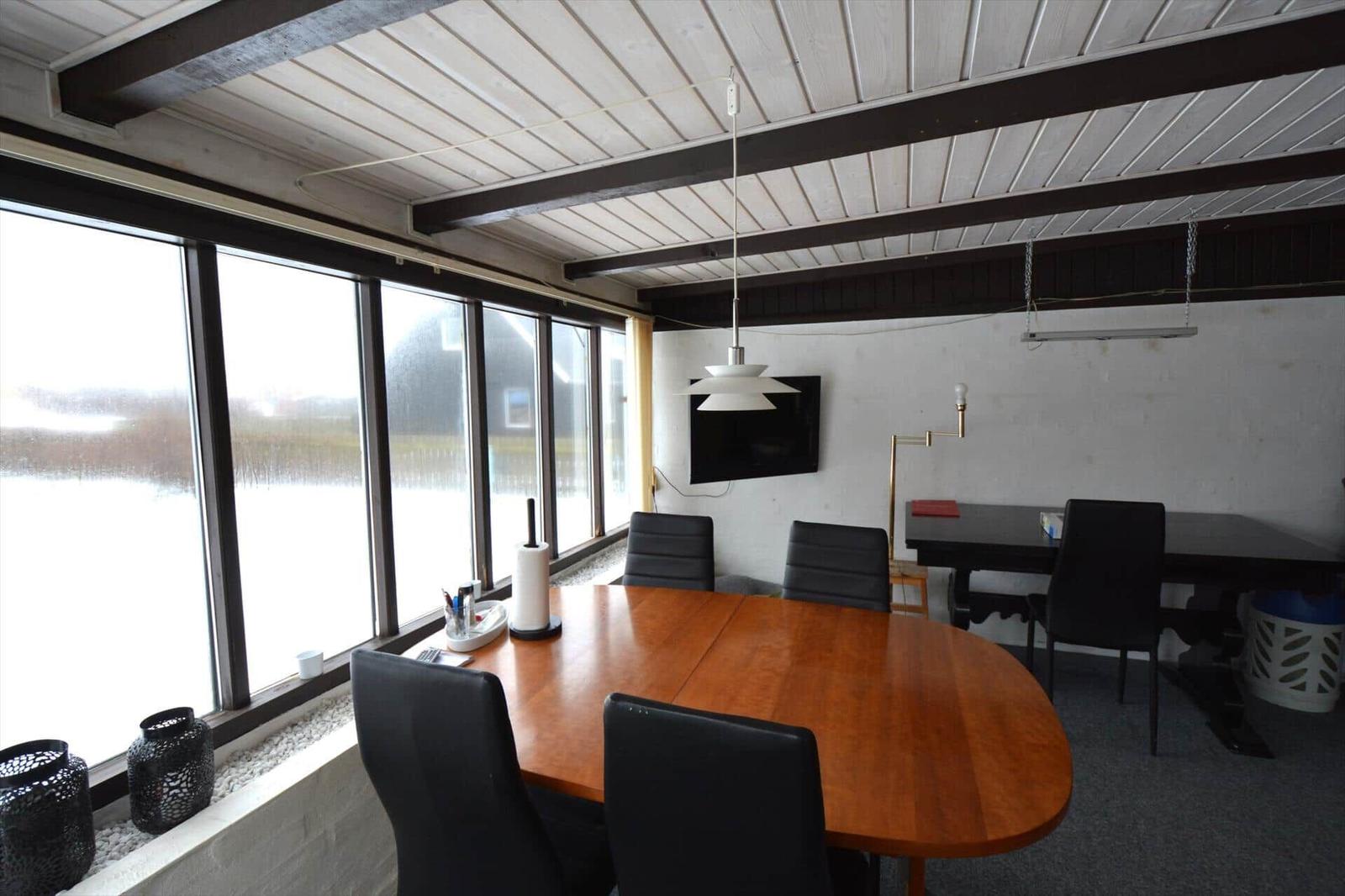 Esszimmer mit Tisch, Stühlen und großen Fenstern. Decke mit Holzbalken und Lampe.
