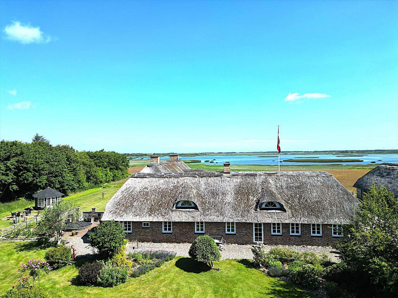 Dorfhaus mit Strohdach und Garten. Blick auf Wasser und Wiesen.