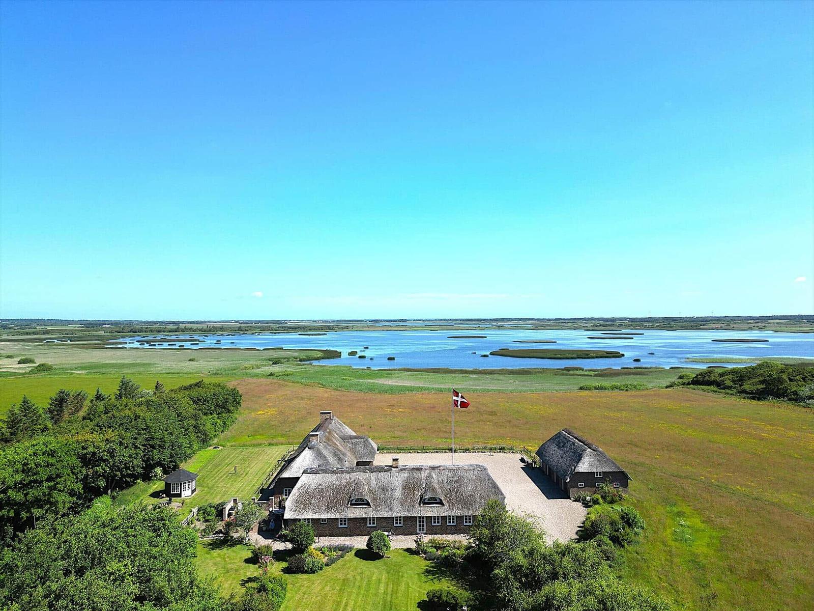 Traditionelle Dänenhaus mit Dach aus Stroh, umgeben von Wiesen und Wasser.