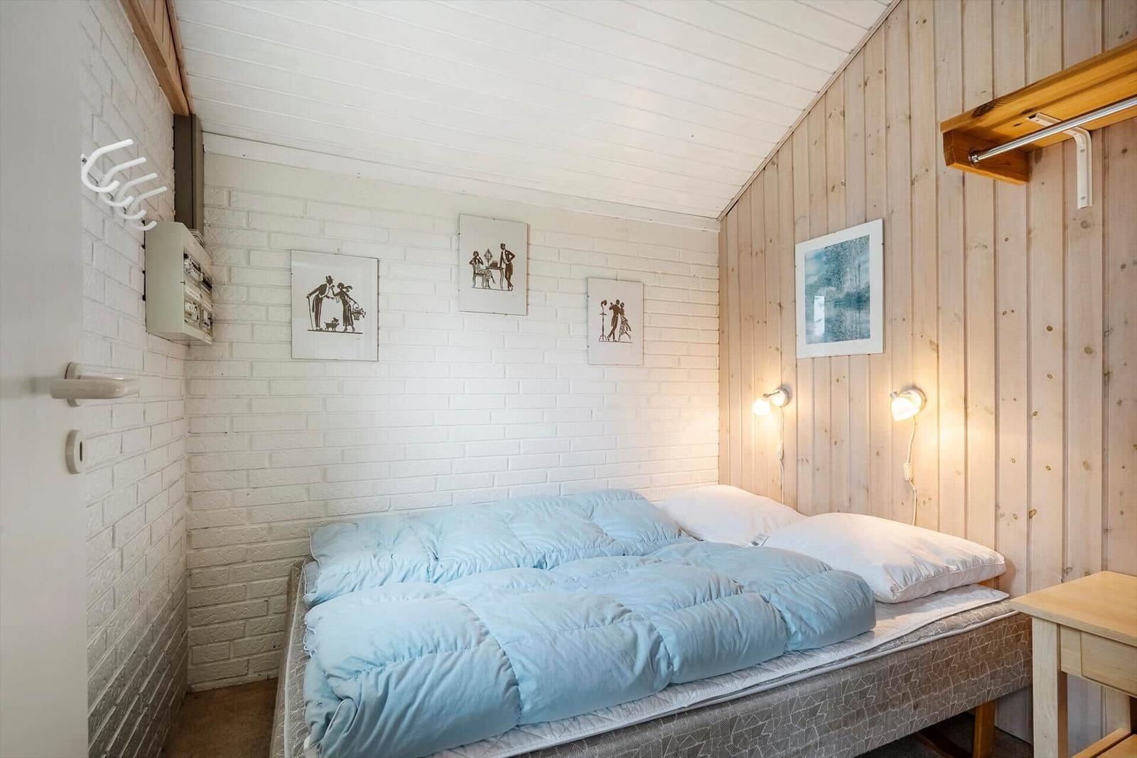 Schlafzimmer mit Bett, Holzwand und weißen Ziegelwand. Bilder an der Wand. Nachttische mit Lampen.