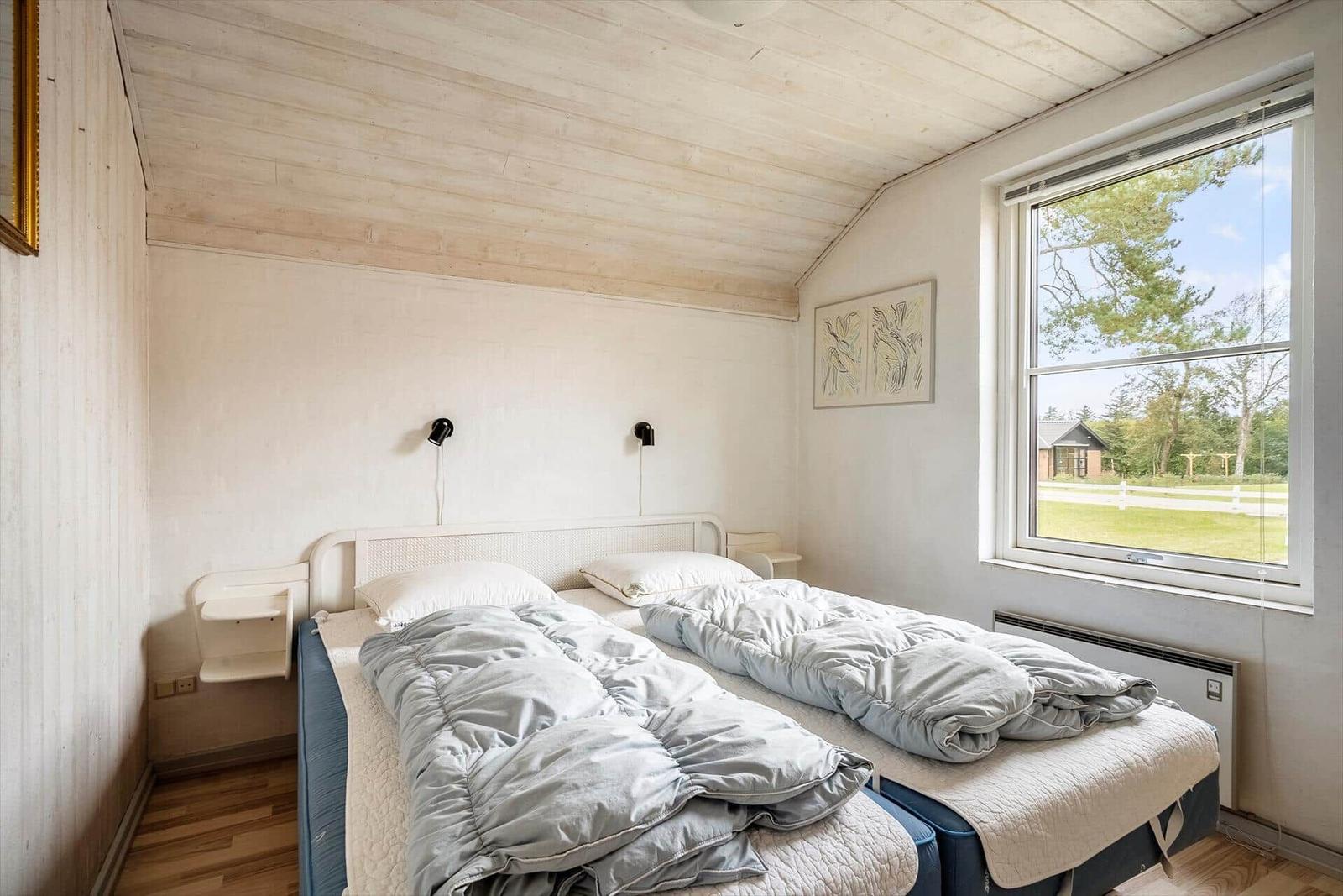 Zwei Betten mit grauen Decken, Fenster mit Blick auf Grünfläche und Bäume.