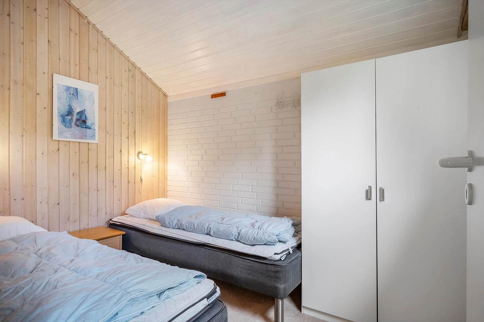 Zwei Betten, weiße Schrankwand und Holzwand im Schlafzimmer.