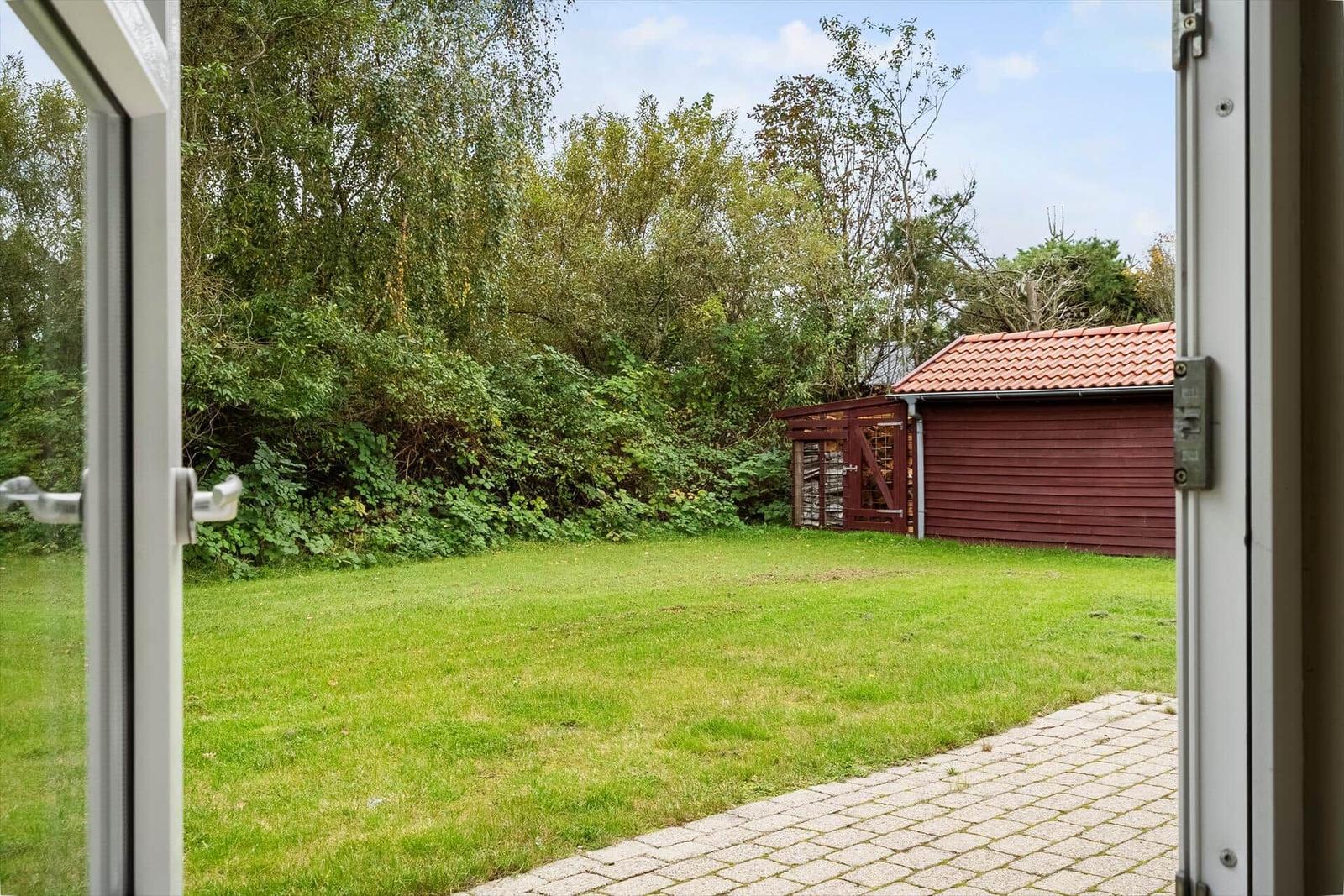 Grüner Garten mit Steinweg und rotem Holzschuppen im Hintergrund.
