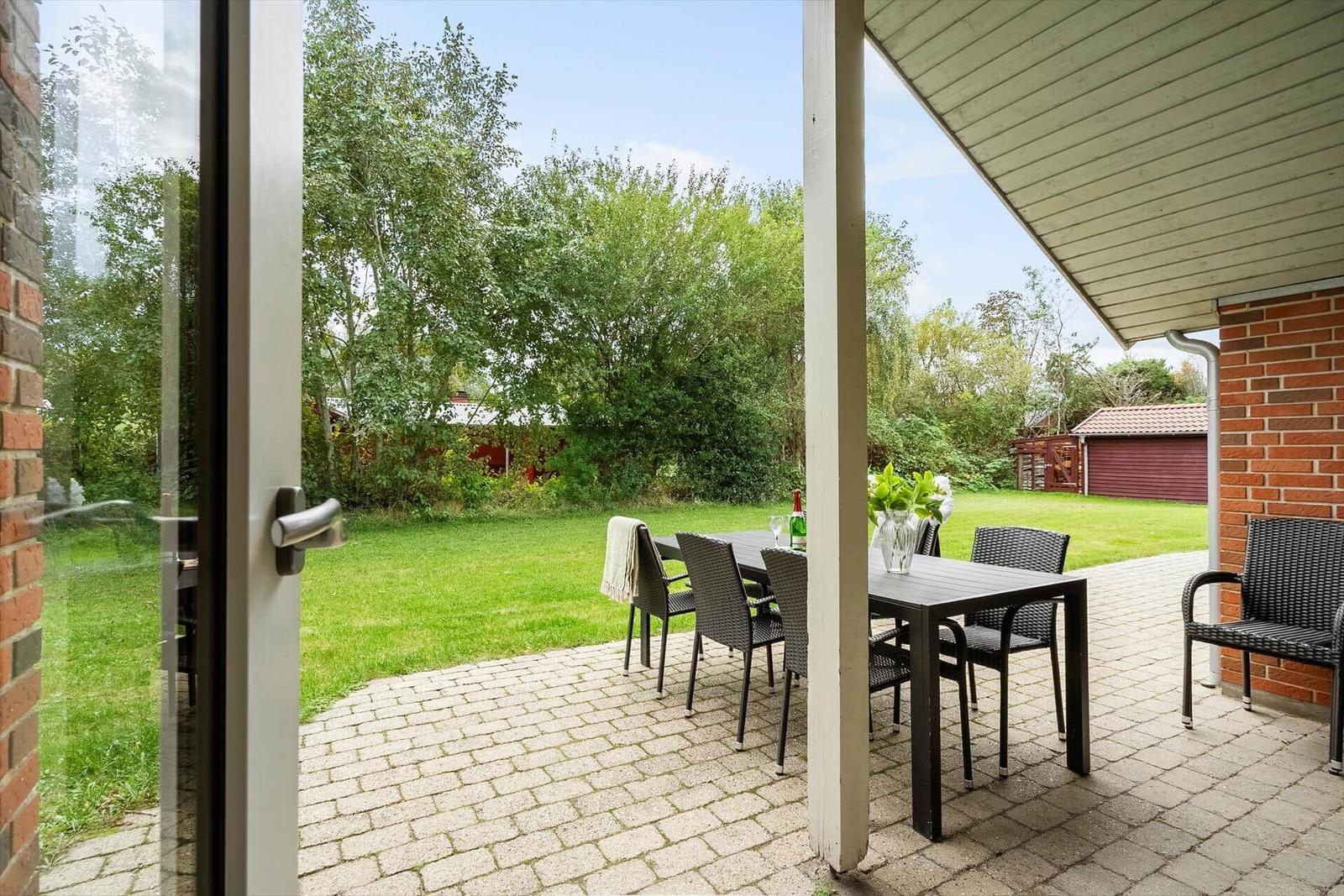 Terrasse mit Tisch und Stühlen, Blick auf grünen Garten und roten Schuppen.