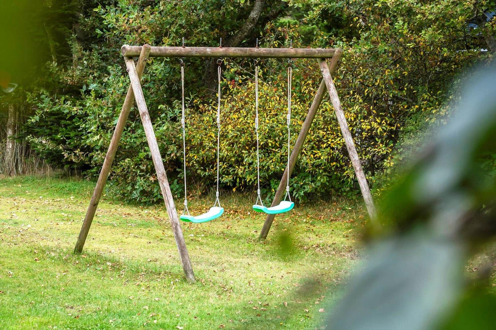 Holzschaukel mit zwei grünen Sitzplätzen im Garten.