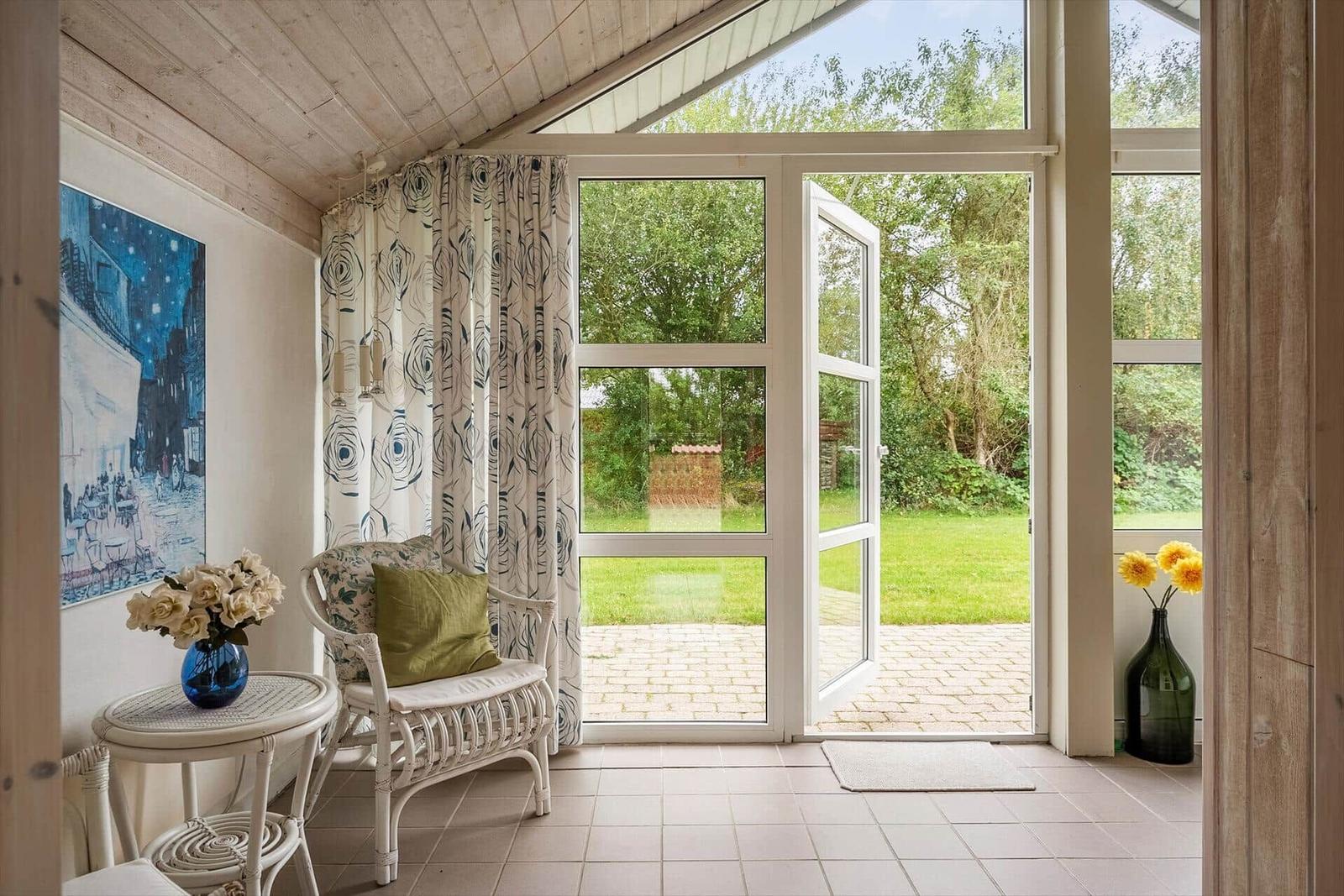 Ein Raum mit weißen Möbeln, Vorhängen und einer Glastür zum Garten.