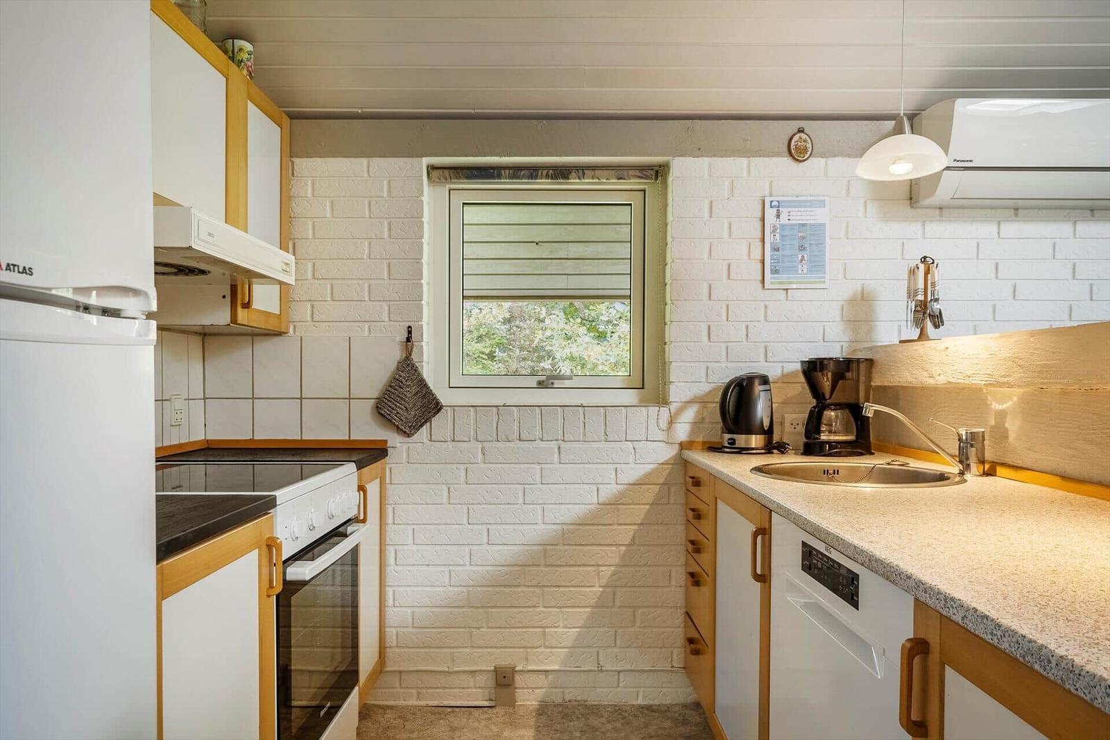 Küche mit Kühlschrank, Herd und Spüle an weißer Ziegelwand.