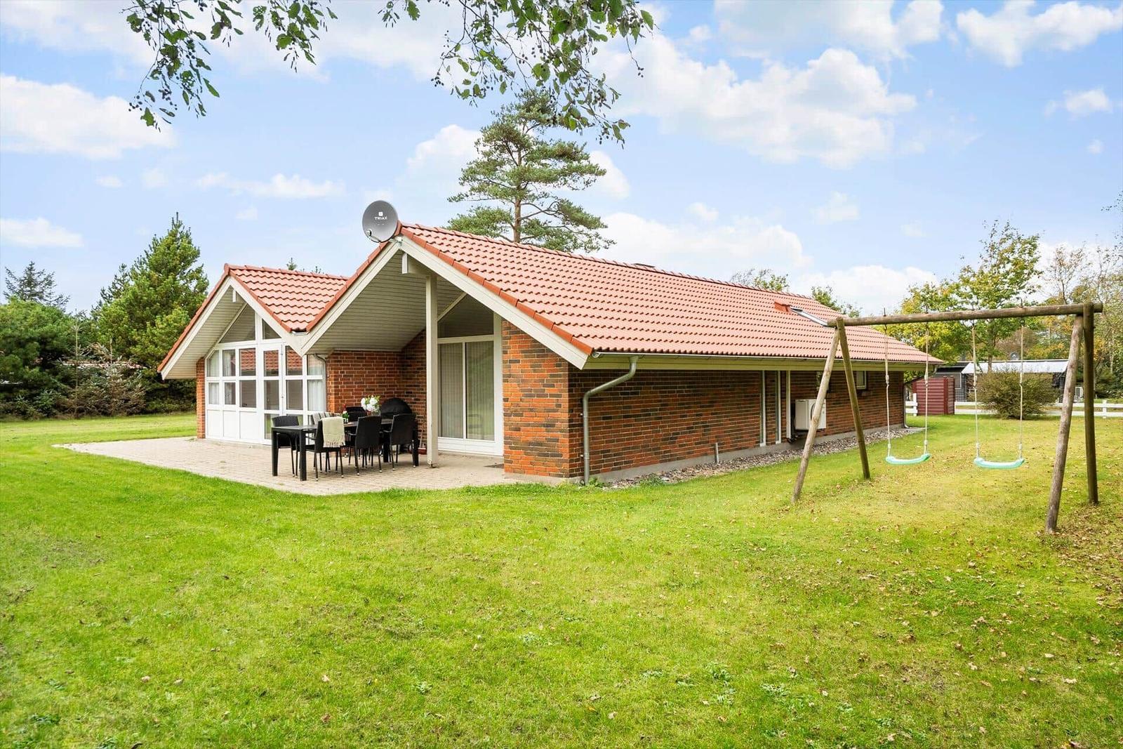 Ein Haus mit Terrasse, Grill und Schaukel im Garten.