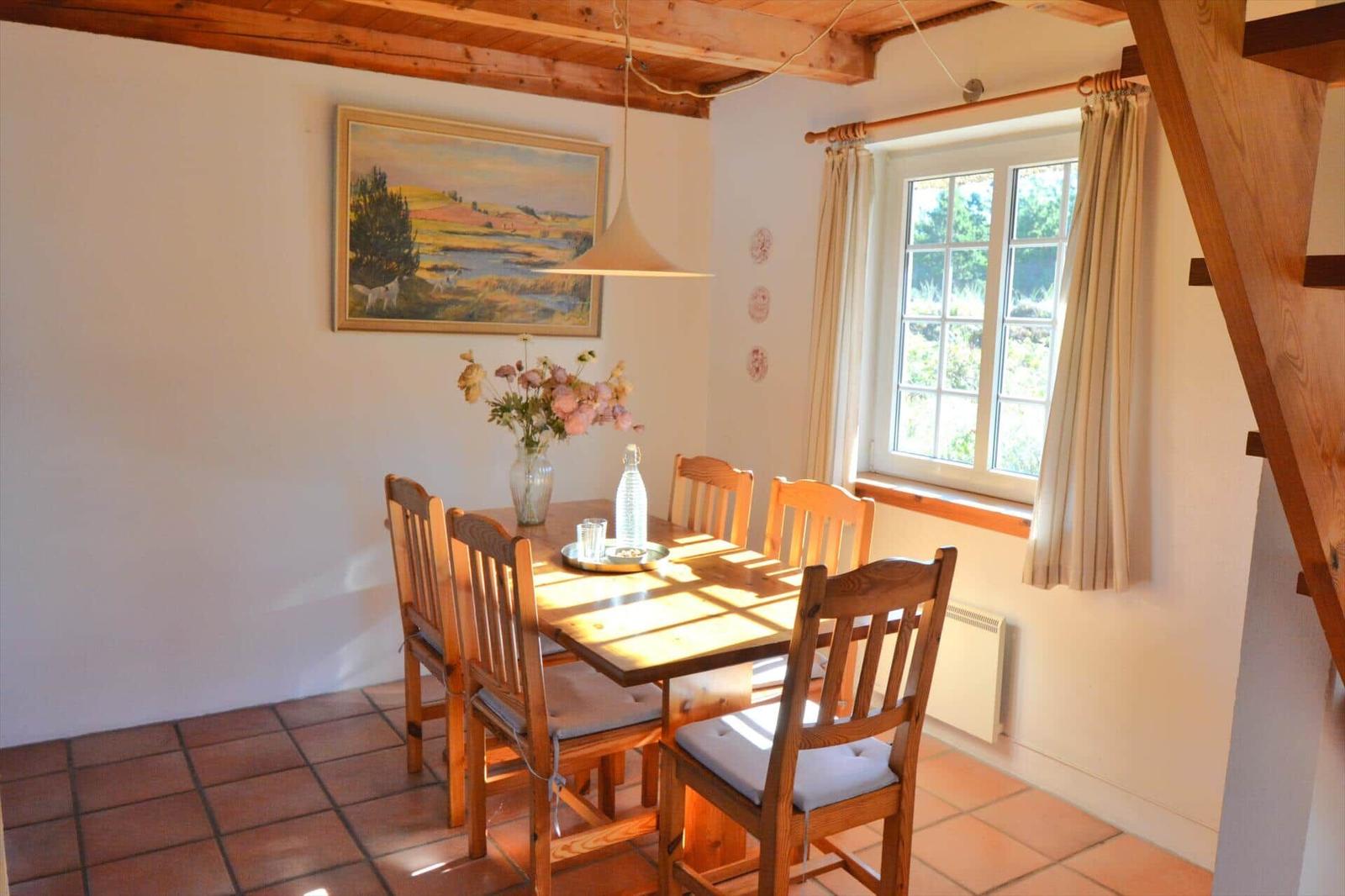 Esszimmer mit Holztisch, Stühlen und Fenster. Holzdecke und Fliesenboden.