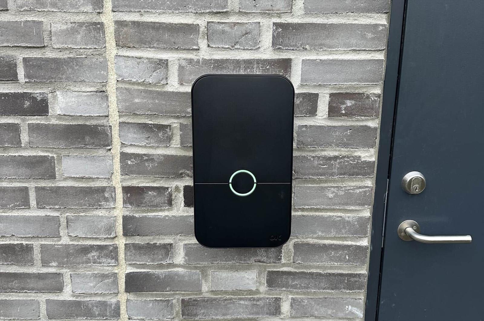Schwarze Türöffneranlage an grauer Ziegelwand neben dunkler Tür