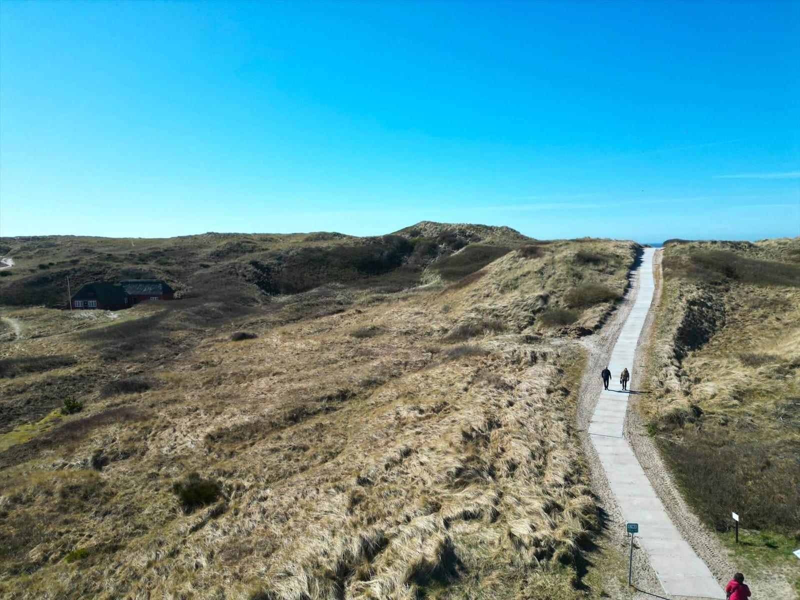 Weg durch Dünenlandschaft mit Blick auf Haus und Meer