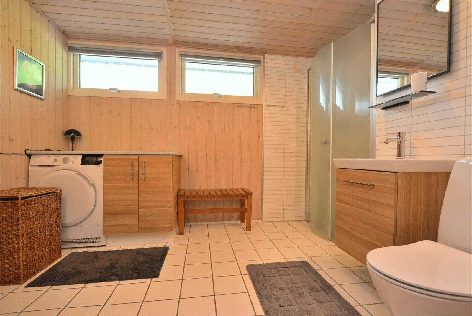 Badezimmer mit Dusche, Waschmaschine und Holzmöbeln.