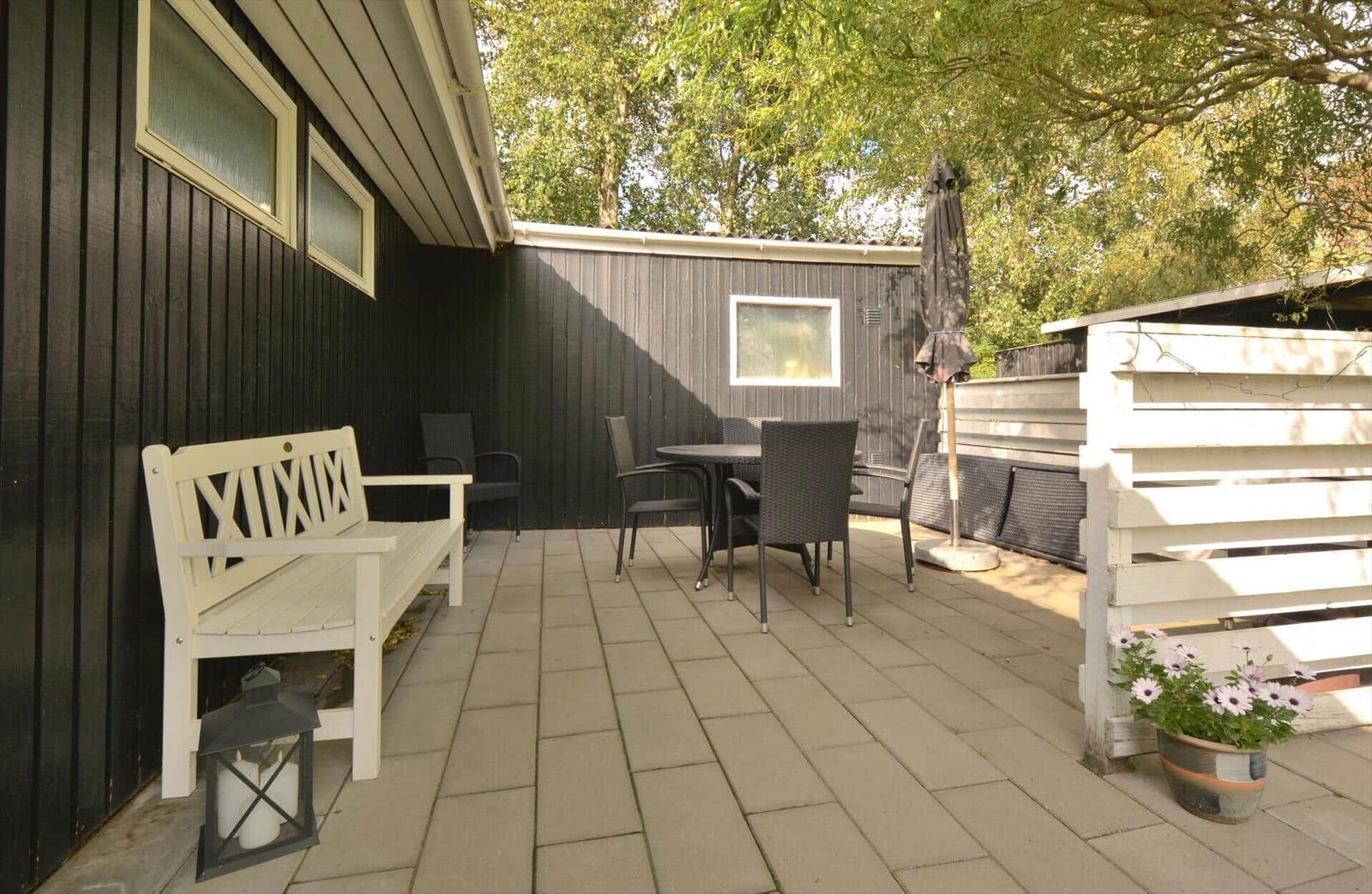 Terrasse mit weißem Bänke, Tisch und Stühlen, Pflanze und Sonnenschutz.