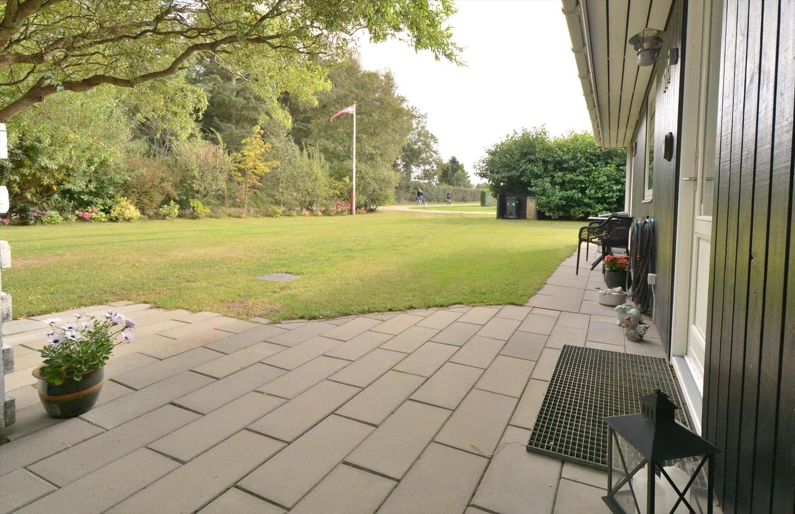 Terrasse mit Pflanzen und Blick auf grünen Rasen und Flagge.