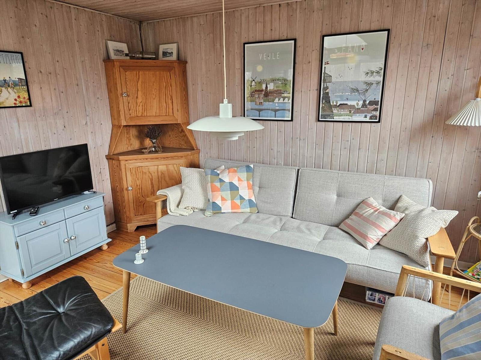 Wohnzimmer mit Sofa, Couchtisch und Fernseher. Holzwände und Bilder an der Wand.