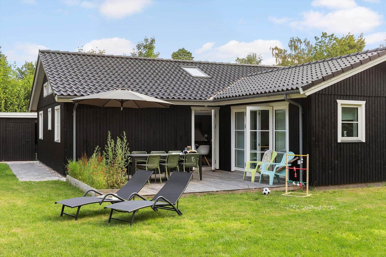 Schwarzes Haus mit Terrasse, Liegestühlen und Garten.