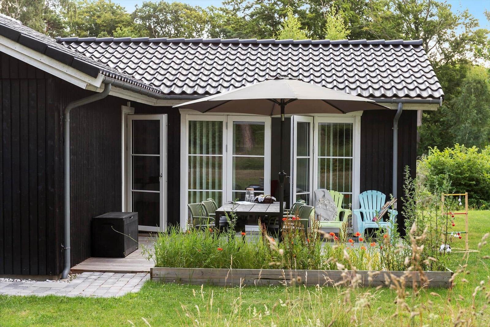 Haus mit Terrasse, Garten und Sitzgelegenheiten unter Sonnenschirm.