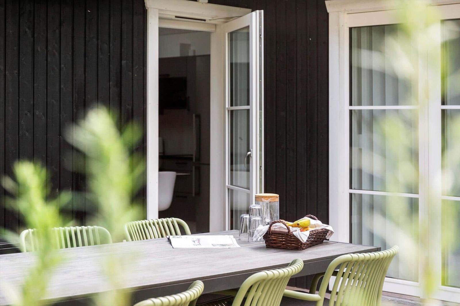 Außenbereich mit Tisch und Stühlen vor einem Haus mit offenen Türen.