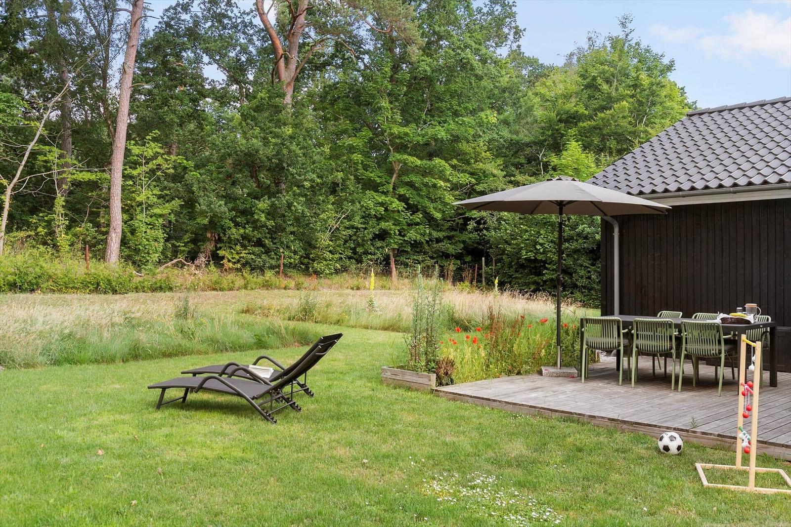 Hinterhof mit Liegestühlen, Terrasse, Tisch, Stühlen und Sonnenschirm.