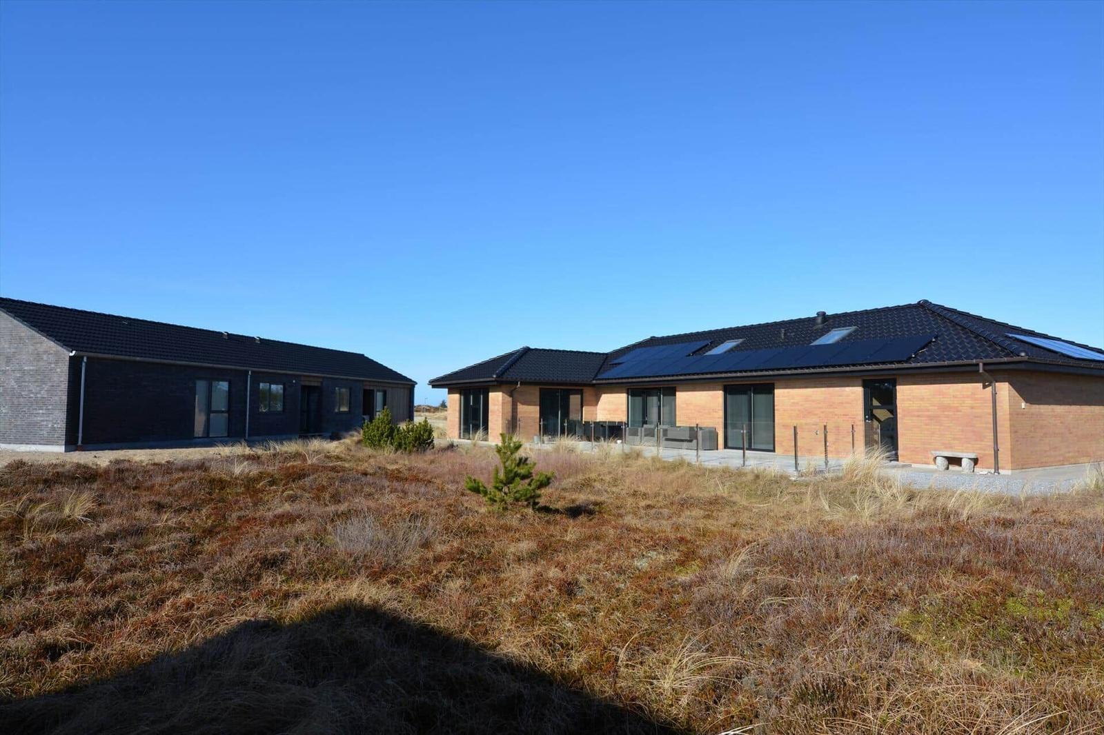 Zwei moderne Häuser mit dunklem Dach und großen Fenstern stehen auf einer grasbewachsenen Fläche.