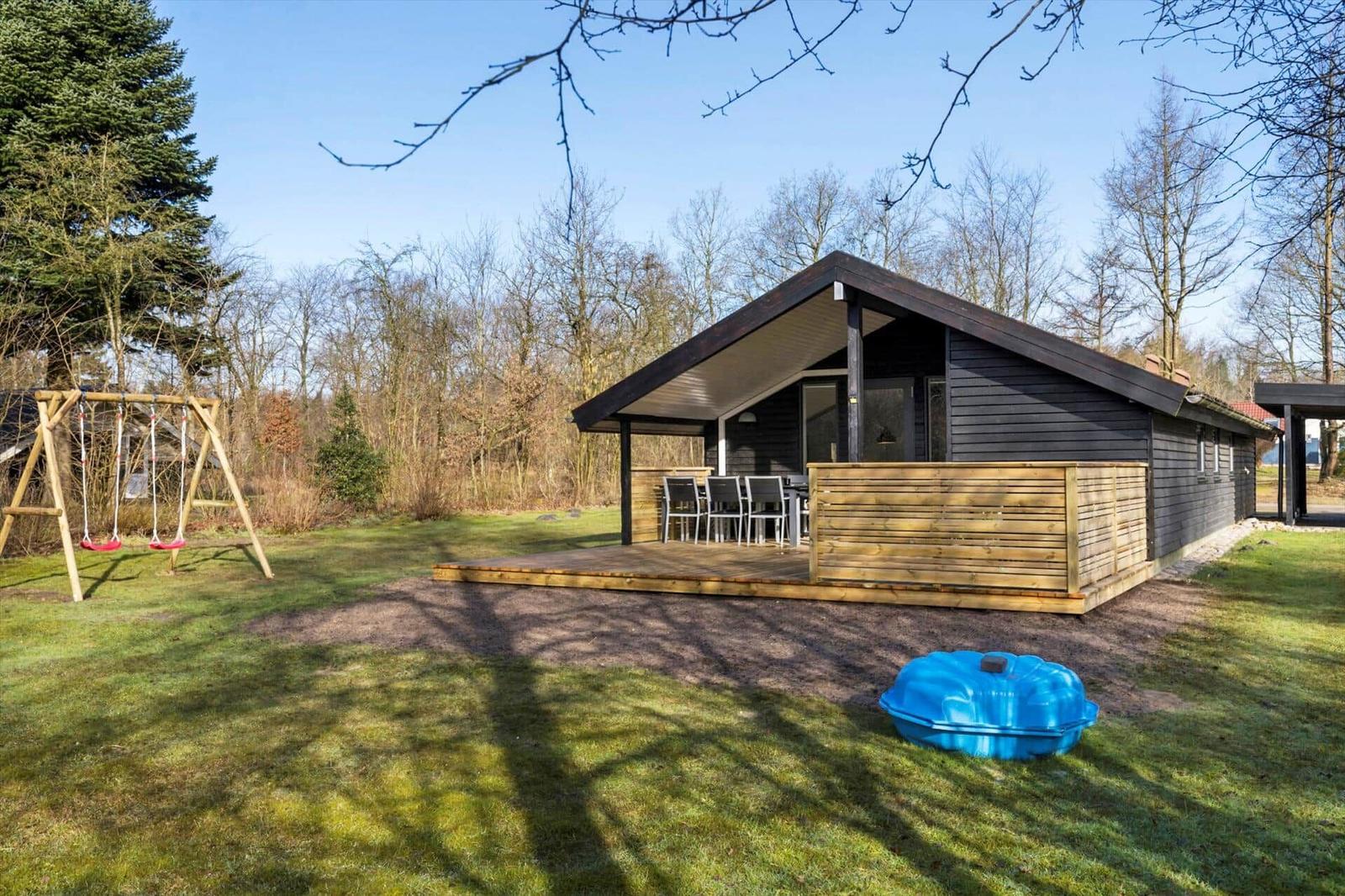 Moderne Holzhütte mit Terrasse, Spielplatz und blauem Pool im Grünen.