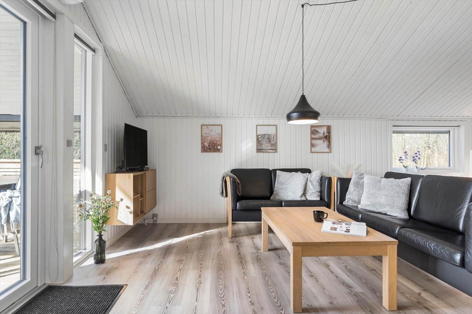 Wohnzimmer mit schwarzen Sofas, Holztisch und Fernseher an der Wand.