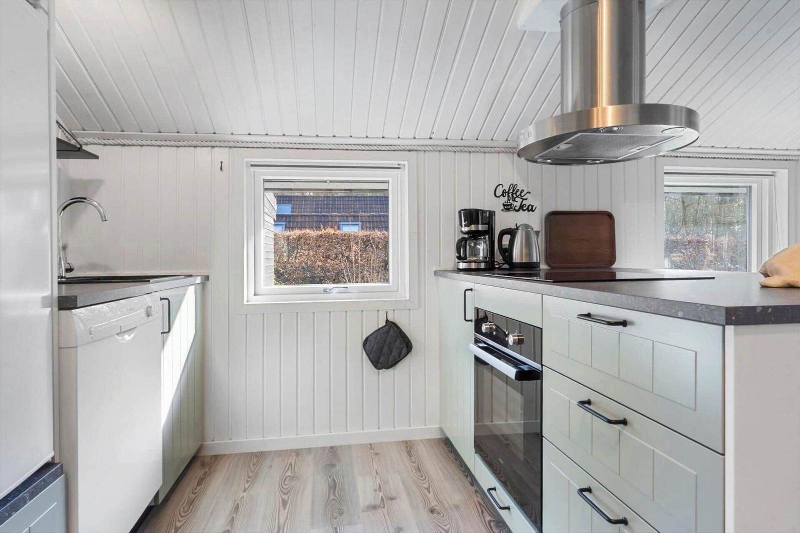 Küche mit weißen Schränken, Edelstahlherd und Fenstern.