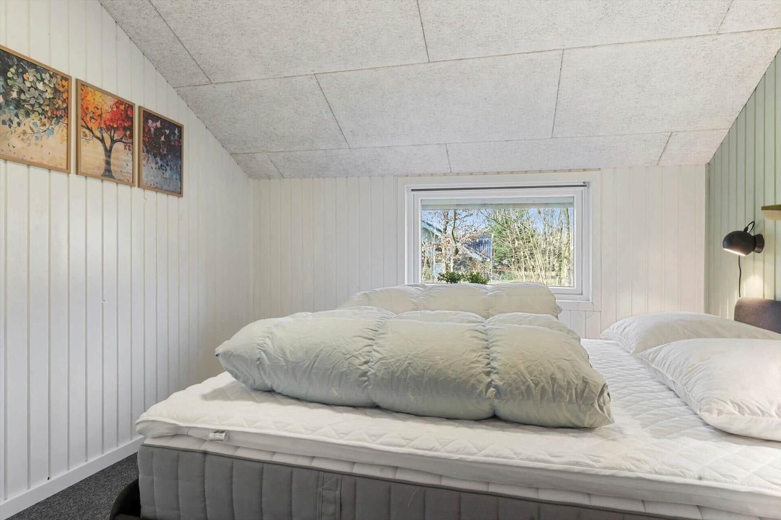 Schlafzimmer mit Bett, Fenster und Wandbildern.