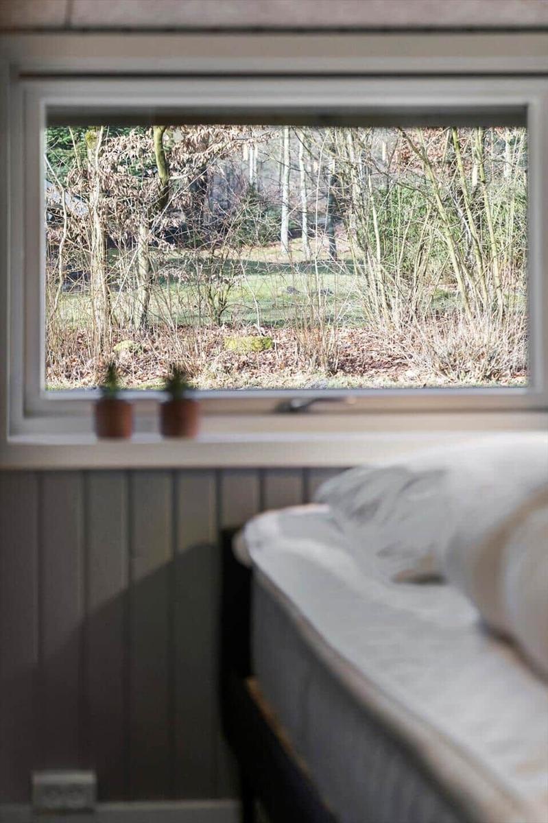 Ein Bett vor einem Fenster mit Blick auf einen Wald.